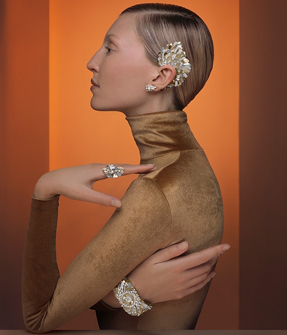 Woman standing in front of an orange background, showcasing a metallic silver and golden ring and earring.