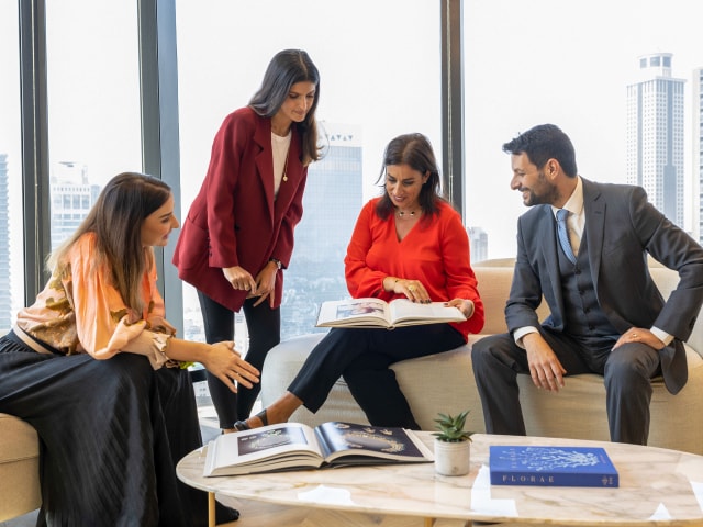 A group of workers reviewing printed documents and magazines in a meeting room with a city view in Dubai