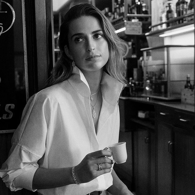 Woman model drinking a coffee with Buccelati necklace, bracelet and ring 
