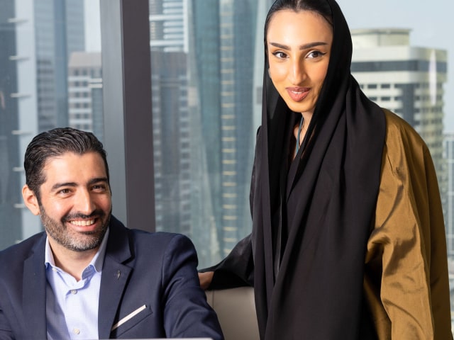 A woman and a men smiling in the conference room with a view over the city of Dubai