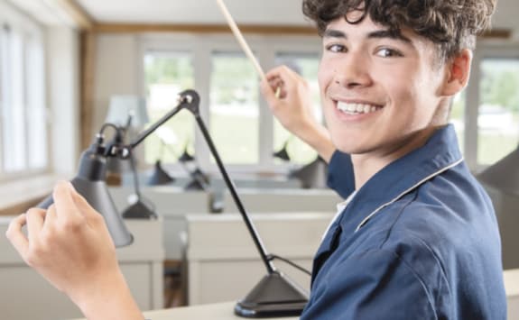 An apprentice working on a watch in a workshop and smiling